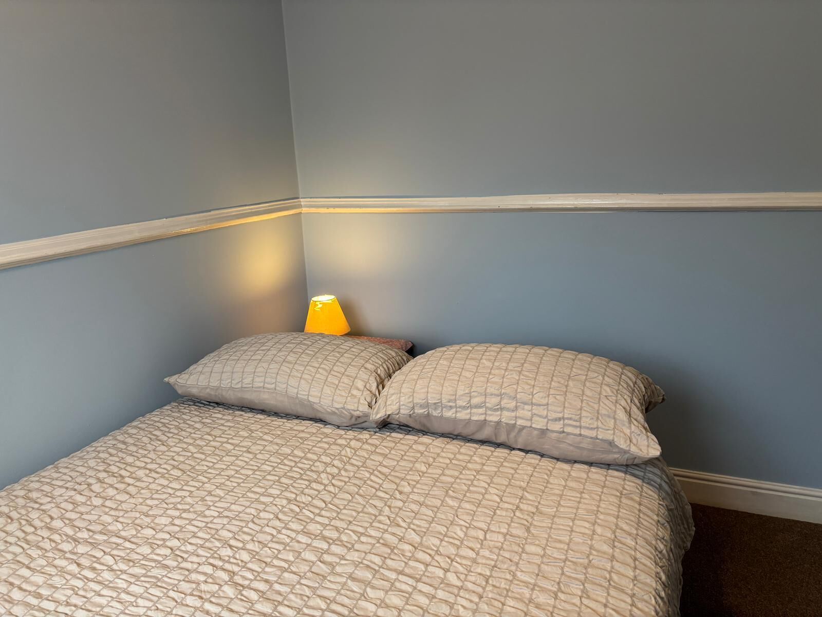 Un dormitorio con una cama, dos almohadas y una mesita de noche con una lámpara.