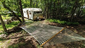 A hammock in a forested area with a small cabin in the background. - Outlier Inn Vintage Trailer Upstate Catskills Farm (Woodridge)
