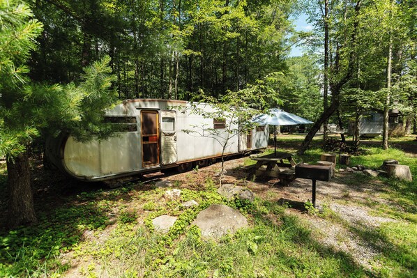 A vintage train car converted into a stationary home, surrounded by trees and a picnic table.