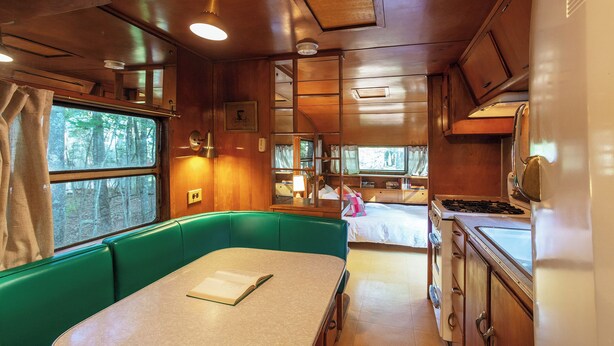 A compact RV interior with a dining area, kitchenette, and a bed. - Outlier Inn Vintage Trailer Upstate Catskills Farm (Woodridge)