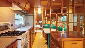 A compact RV kitchen with a stove, sink, and a dining area. - Outlier Inn Vintage Trailer Upstate Catskills Farm (Woodridge)