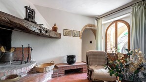 A cozy living room with a fireplace, a comfortable sofa, and a view through an arched window. -  Casa La Cedrina Pool Lornano (Monteriggioni)