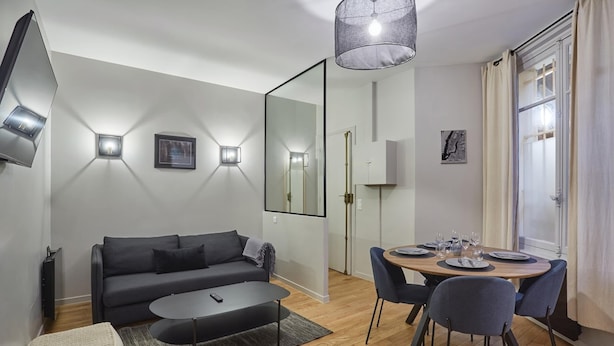 A modern living room with a sofa, coffee table, and dining area with chairs and a table set for four. - Apartment in the Center of Paris-sacre Coeur (Paris)