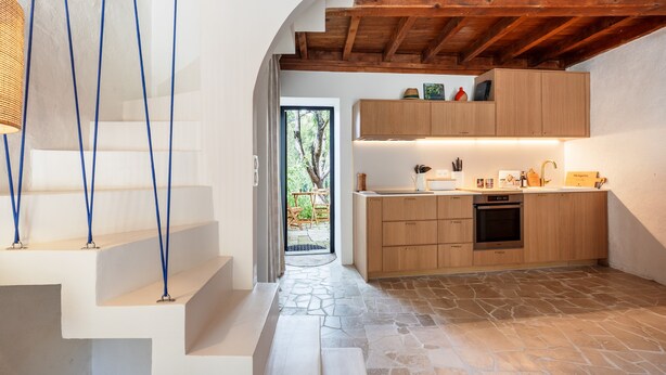 A modern kitchen with wooden cabinets, a built-in oven, and a stone-tiled floor.