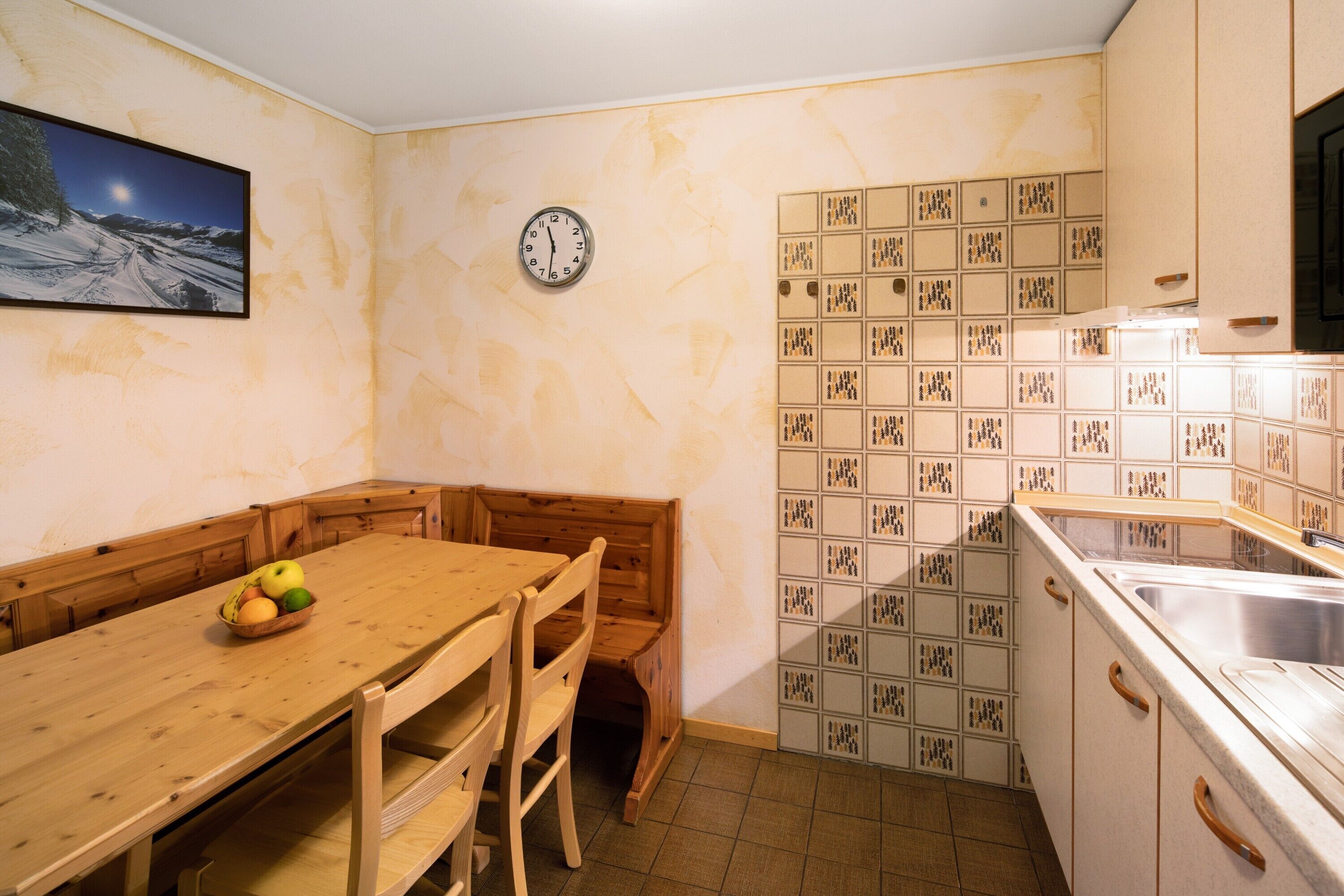 A kitchen with a wooden table, chairs, a clock, and a tiled backsplash.