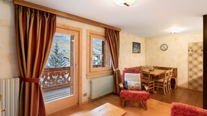 A cozy room with a wooden table, a red chair, and a view of a snowy landscape through large windows. - Apartment '2' with Mountain View, Balcony and Wi-Fi (Livigno)