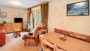 A cozy living room with a wooden dining table, a sofa, a television, and a window with curtains. - Apartment '2' with Mountain View, Balcony and Wi-Fi (Livigno)