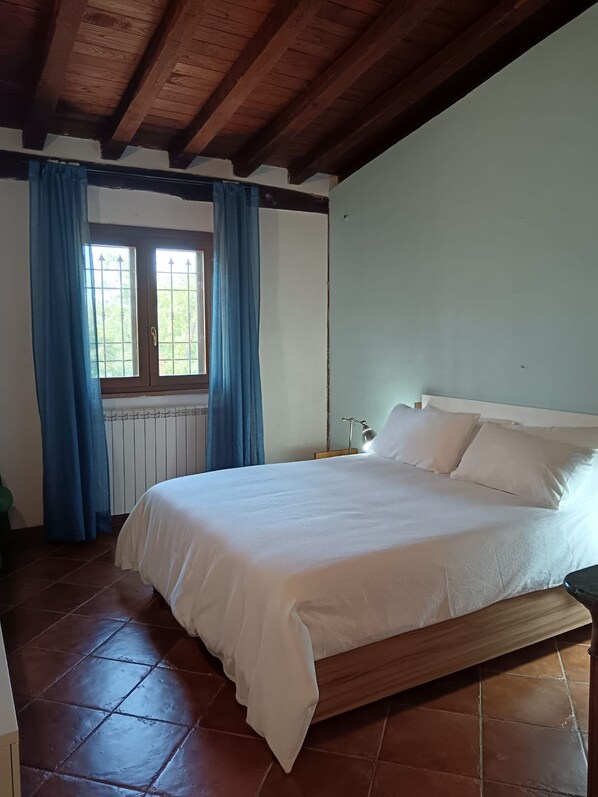 Una camera da letto con un letto in legno, biancheria da letto bianca e una finestra con tende azzurre.