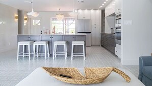 Een moderne keuken met witte kasten, een centraal eiland met krukken, en hangende verlichting.