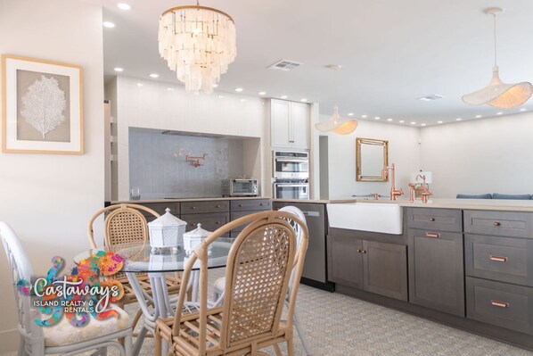 A modern kitchen with grey cabinets, stainless steel appliances, and a glass dining table with wicker chairs.