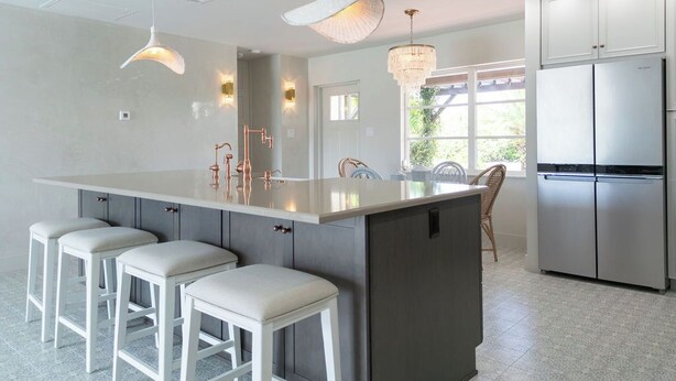 Een moderne keuken met een groot eiland, barkrukken, roestvrijstalen apparatuur, hanglampen en uitzicht op het buitengebied.