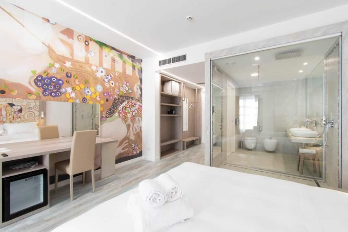 Una habitación de hotel moderna con cama, escritorio, silla, armario y baño con cabina de ducha de vidrio.