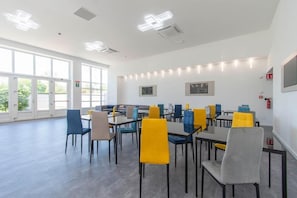 A spacious room with multiple tables and chairs, large windows, and ceiling lights. - Max Motel - Art Gallery Room  (Druento)