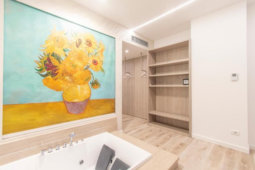 A bathroom with a large painting of sunflowers, a bathtub, and wooden shelving units.