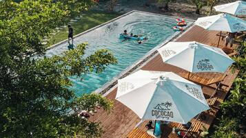 Vue aérienne d’un espace piscine agrémenté de plusieurs parasols sur lesquels on peut lire l’inscription « Cococao Glamping ».