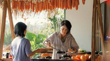 A person cooking on a stove with corn on the cob hanging above.
