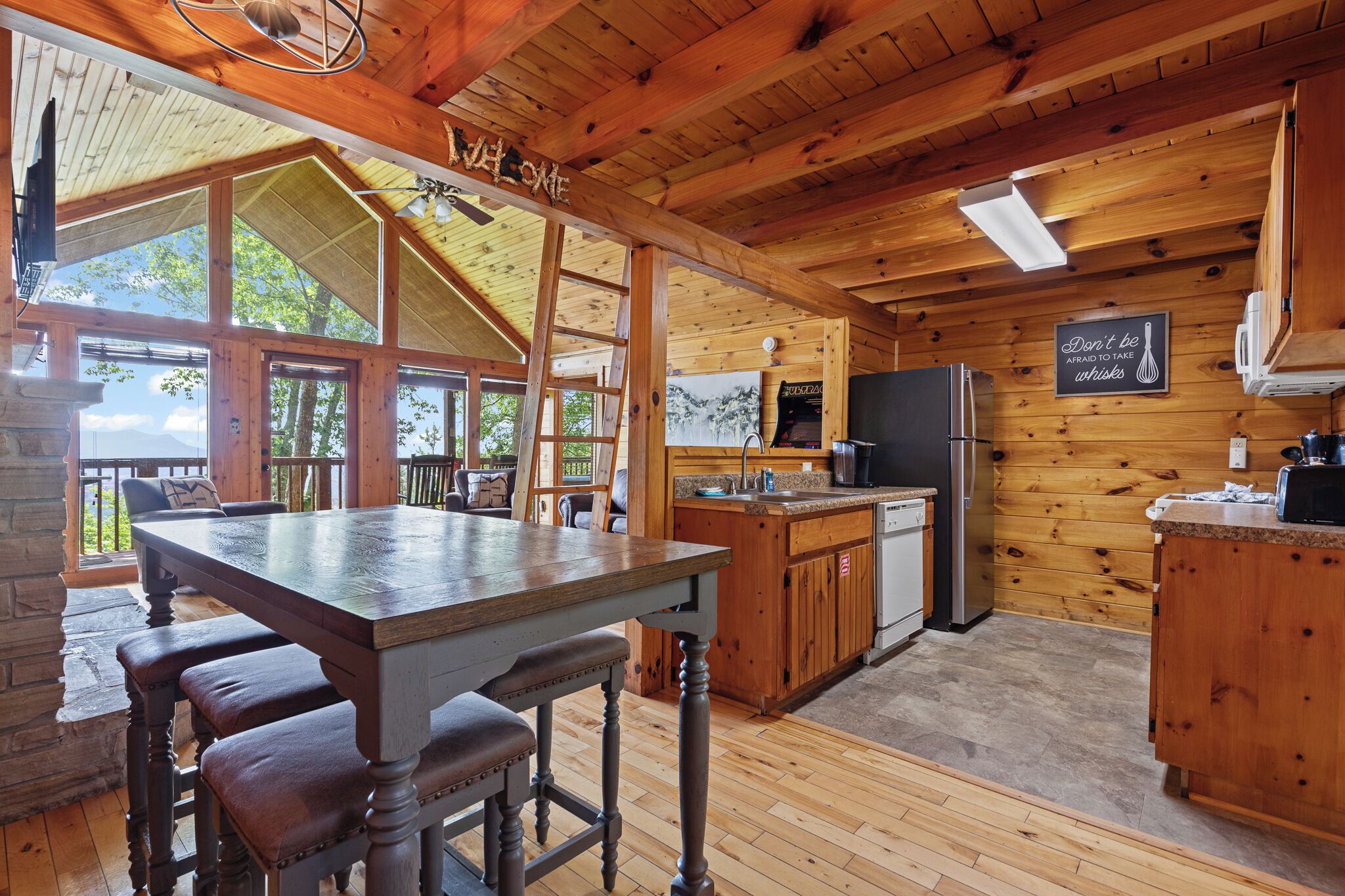 A wooden cabin with a dining area, kitchen, and large windows.