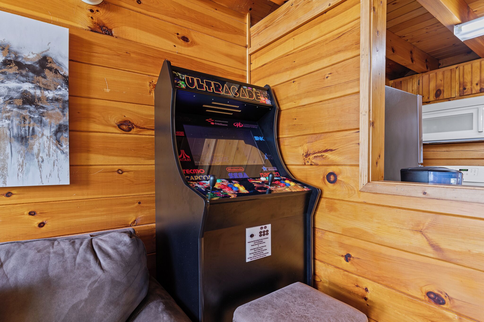 A wooden cabin interior with a retro arcade machine labeled "ULTRAGADE" and a refrigerator.