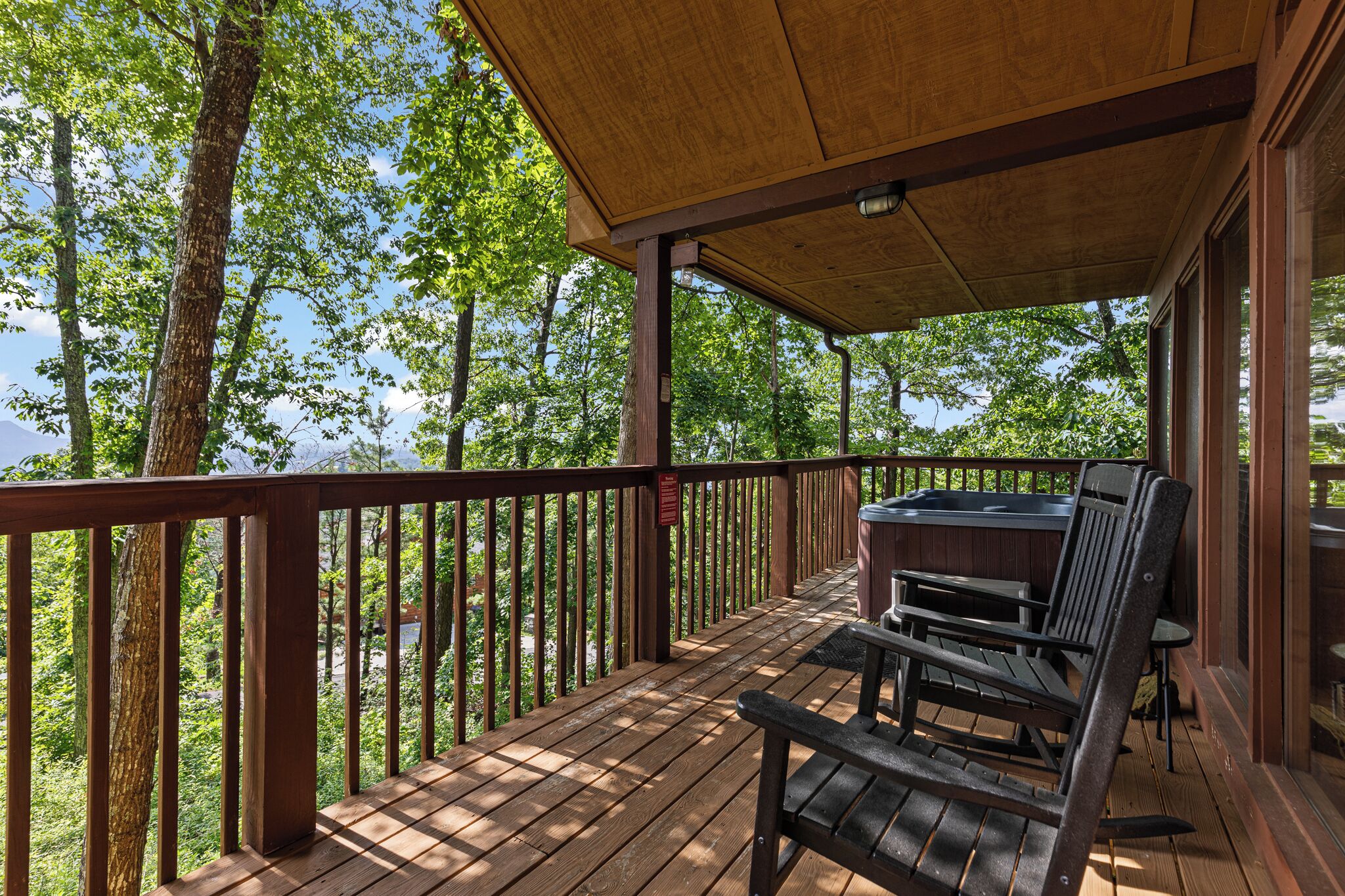 A wooden deck with a covered area, a hot tub, and a chair.
