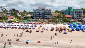 Una playa con agua cristalina, sombrillas y gente. Se ven edificios al fondo.