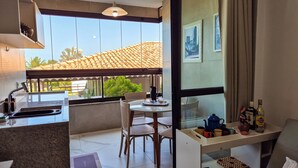 Cocina compacta con lavamanos, comedor con mesa y sillas, y balcón con vista a tejados y vegetación.