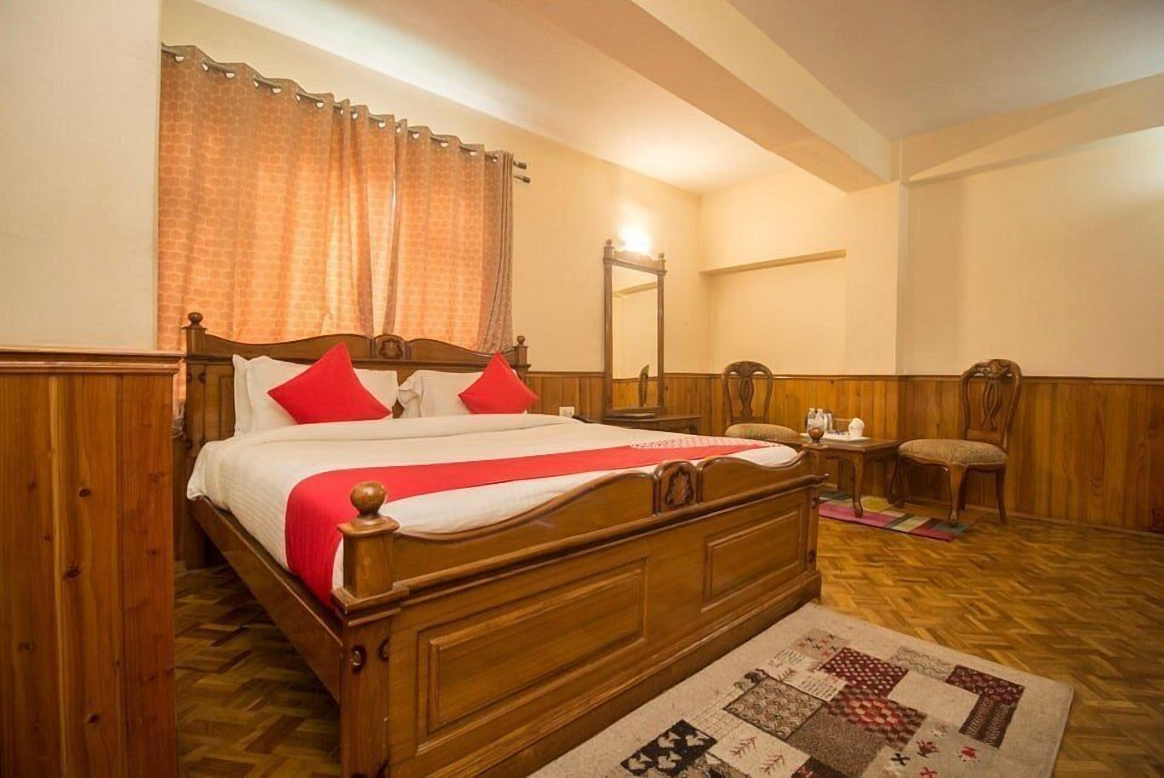 Un lit à baldaquin en bois, avec une literie rouge et blanche, une table de chevet en bois, une chaise et un miroir au mur.