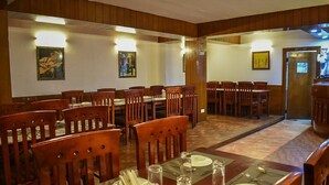 A dining area with wooden tables and chairs, a carpeted floor, and framed artwork on the walls. - Hotel De Villa (Gangtok)