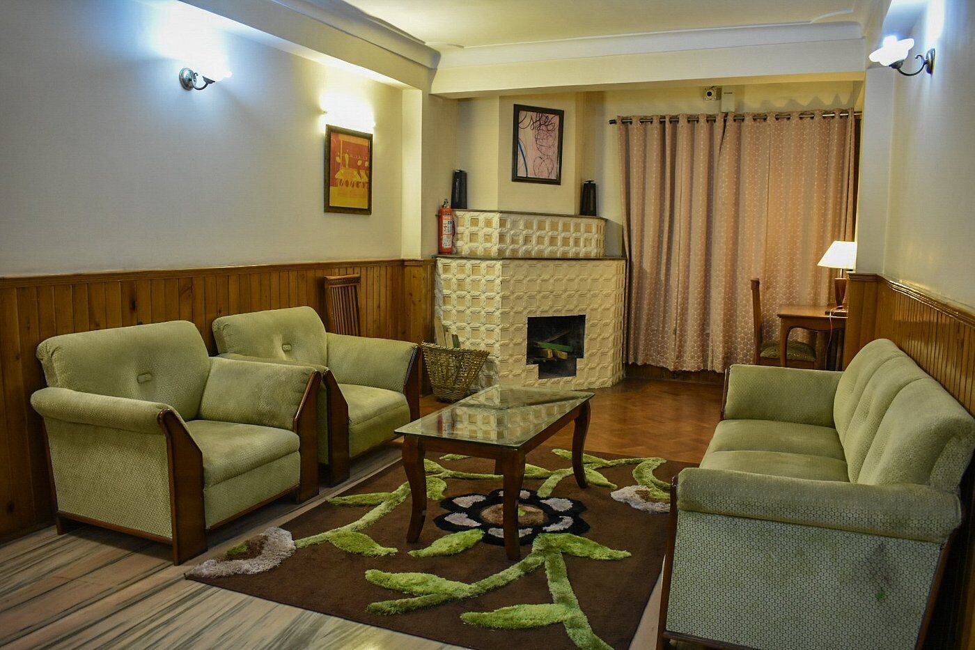 Una sala de estar con dos sillones verdes, una mesa de centro de vidrio, una chimenea y un tapete estampado.
