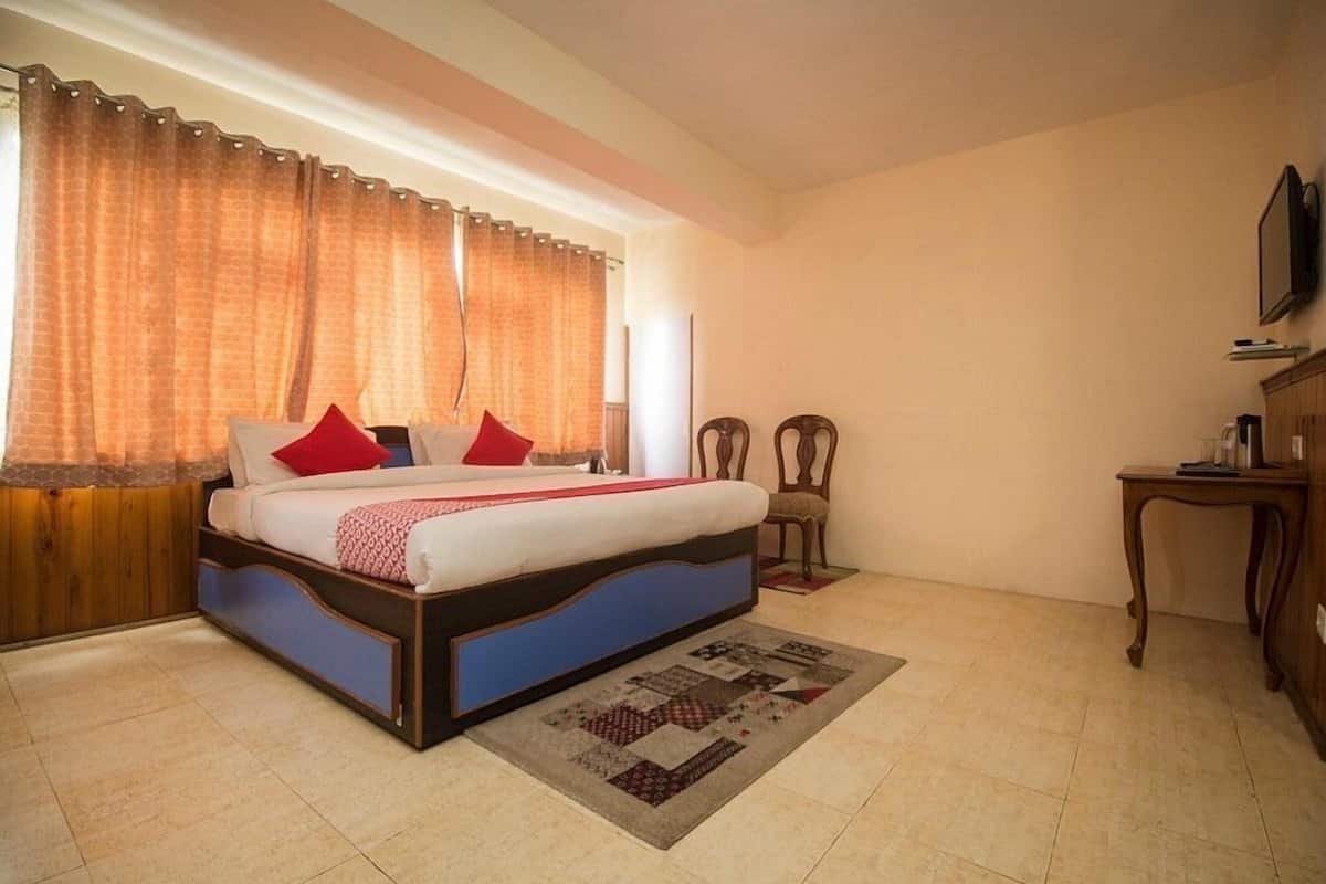 Een slaapkamer met een bed, gordijnen, een stoel, een klein tafeltje en een televisie aan de muur.