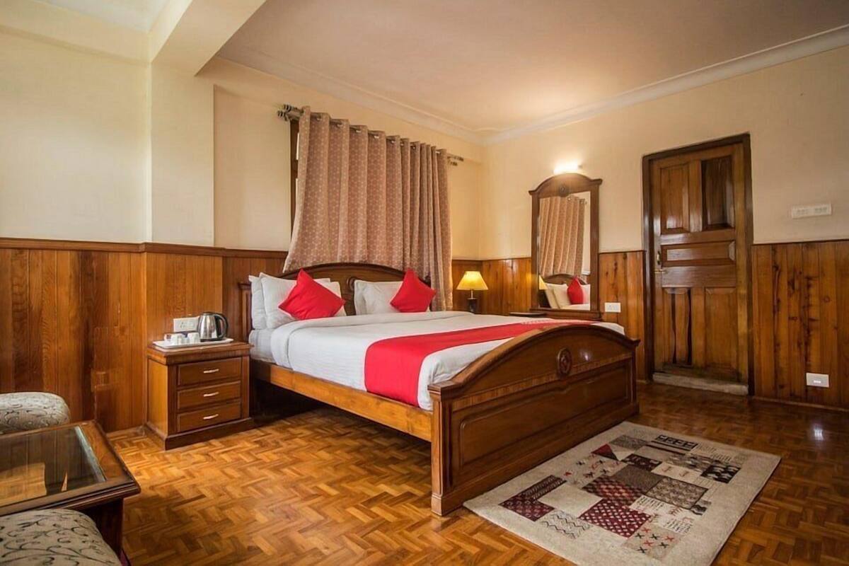 Een slaapkamer met houten frame, met een bed, nachtkastjes, een spiegel en een kamerbreed tapijt met patroon.