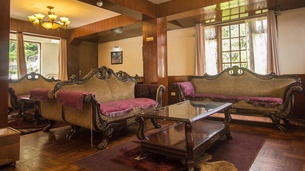 A room with two ornate sofas, a glass coffee table, wooden flooring, and a chandelier. - Hotel De Villa (Gangtok)