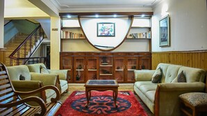 A living room with a staircase, a wooden cabinet with glass doors, and a red patterned rug. - Hotel De Villa (Gangtok)