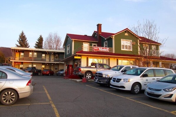 Un motel à la façade verte et au toit rouge, doté d’un parking où sont garées plusieurs voitures.