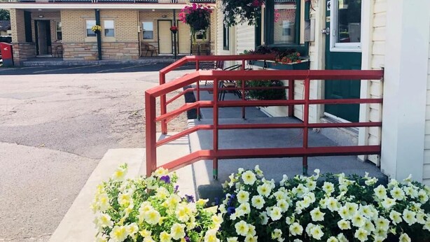 Ein Motel mit einer roten Metalltreppe, die zum Eingang führt, einem überdachten Parkbereich und Blumenkästen mit gelben und weißen Blumen im Vordergrund.