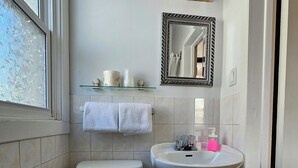 Ein kleines Badezimmer mit Toilette, Waschbecken und Spiegel. Ein Fenster ist vereist, und ein Ablagefach zeigt Toilettenartikel.