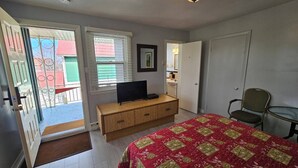 Ein Schlafzimmer mit einem Bett, einem Fernseher auf einer Holzkommode, einem Sessel und einer Tür zu einem Badezimmer.