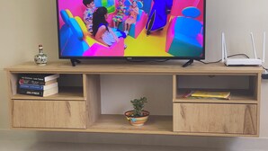 A television on a wooden TV stand with books and a potted plant.