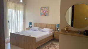 A bedroom with a wooden bed, a nightstand with a lamp, a painting on the wall, and a mirror on the wall.