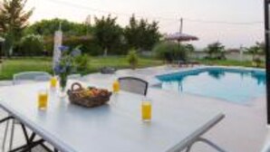 An outdoor pool area with a table set for dining, surrounded by greenery and a clear sky. - Villa Fivos With Private Pool by Lefkadastay (Lefkada)