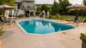 A swimming pool with lounge chairs and umbrellas, surrounded by a house and greenery. - Villa Fivos With Private Pool by Lefkadastay (Lefkada)