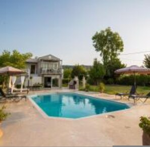 A swimming pool with lounge chairs and umbrellas, surrounded by a house and greenery. - Villa Fivos With Private Pool by Lefkadastay (Lefkada)