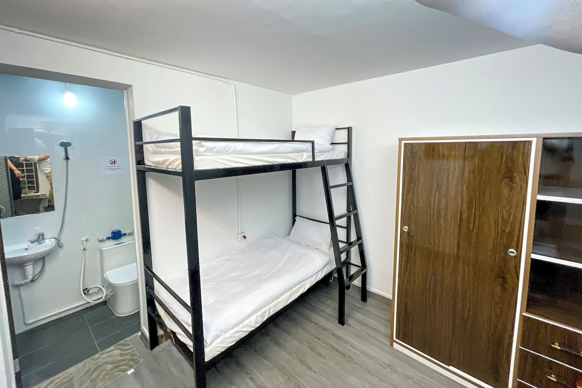A bunk bed room with a wooden wardrobe and a bathroom with a sink and toilet.