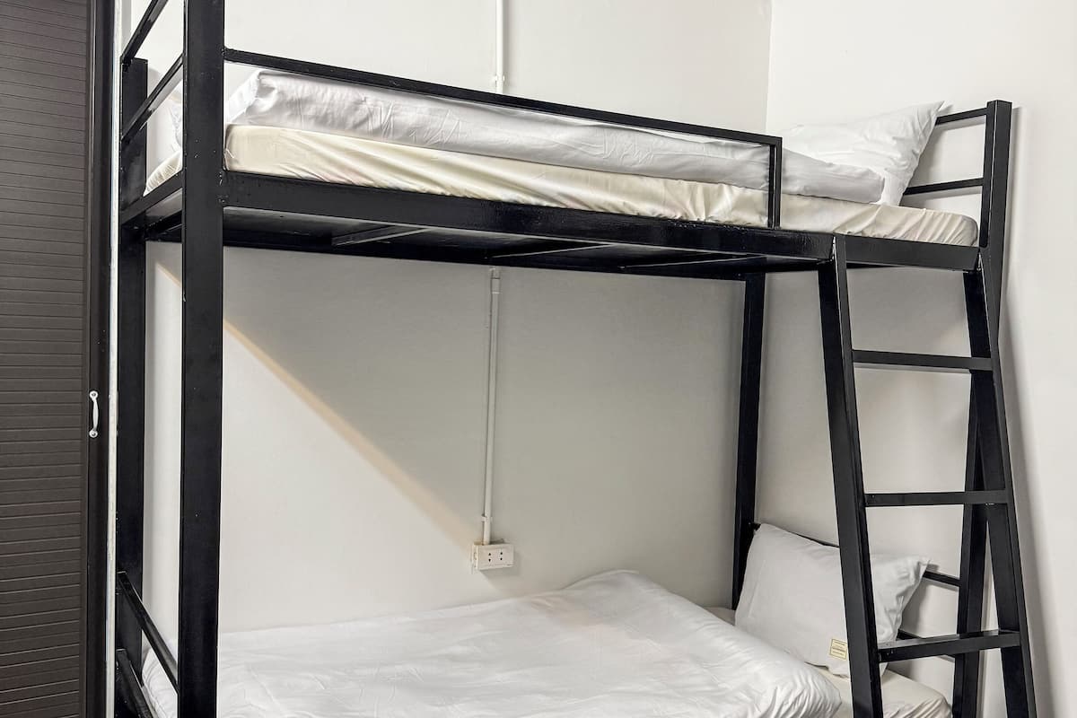 A bunk bed with a ladder, white bedding, and a power outlet on the wall.