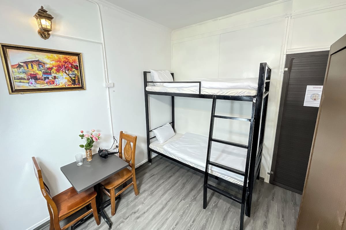 A bunk bed room with a desk and chair, a small table with a vase, and a painting on the wall.