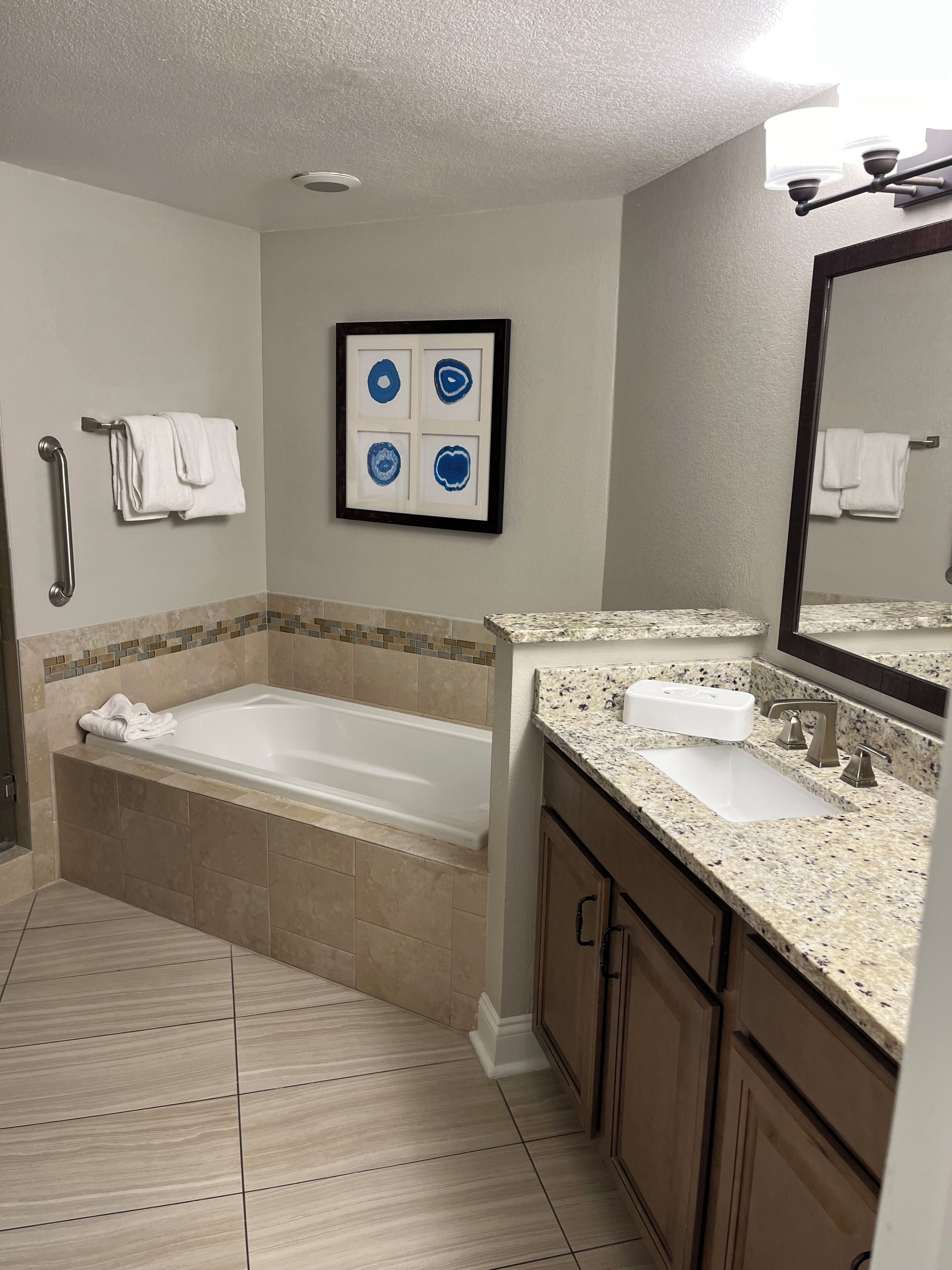 A bathroom with a bathtub, a sink, a mirror, and a framed picture on the wall.