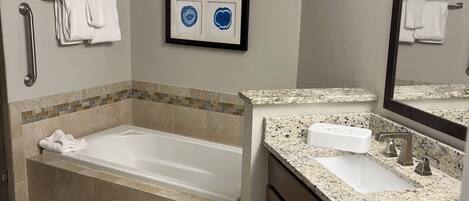 A bathroom with a bathtub, a sink, a mirror, and a framed picture on the wall.