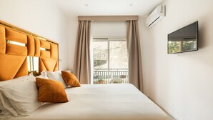 Une chambre d’hôtel avec un lit, des rideaux, un appareil de climatisation, une télévision et une fenêtre donnant sur un paysage agréable.