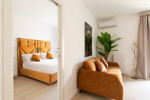 A modern hotel room with a bed, sofa, and a large plant.