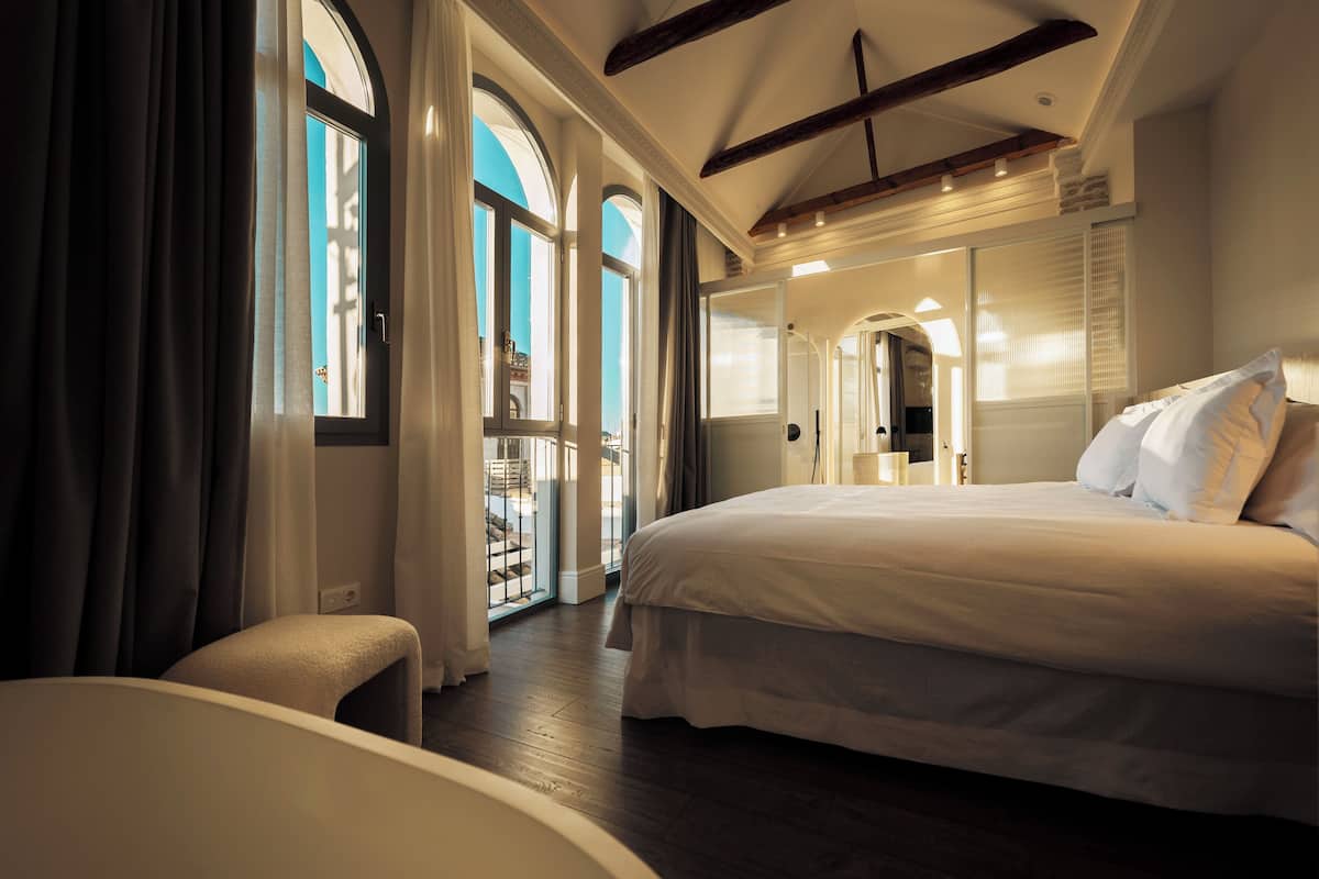 A spacious bedroom with a large bed, a sitting area, and a view of the outdoors through a glass door.