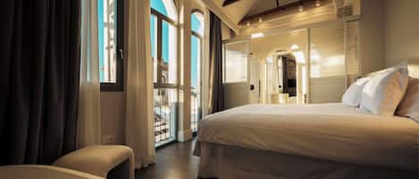 Un dormitorio amplio con una cama grande, una zona de estar y vistas al exterior a través de un ventanal.